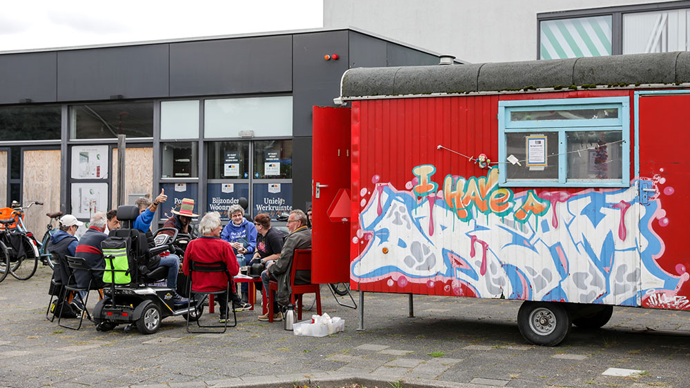 Groepje mensen zit buiten naast een woonwagen